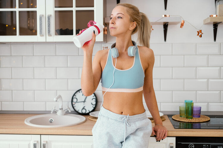 Vrouw drinkt een eiwitshake in de keuken als onderdeel van afvallen met eiwitshakes en een gezonde leefstijl.
