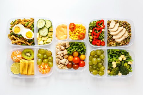Assortment of six meal prep containers filled with a variety of healthy foods on a white background. Top row includes whole grain pasta with boiled eggs, cucumbers and an orange sauce; cherry tomatoes with yellow bell peppers; quinoa with sliced chicken breast and red bell peppers. Bottom row features kiwi slices with green grapes, lime and corn; oatmeal with green beans, chicken chunks and cherry tomatoes; green grapes with broccoli and cubed cheese. This image emphasizes a balanced and colorful meal planning concept.